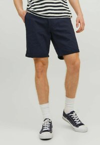 Granatowe bawełniane szorty z podwiniętymi nogawkami, noszone z białymi skarpetami typu crew i granatowymi sneakersami, w połączeniu z prążkowanym t-shirtem z krótkim rękawem.