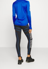 Sininen pitkähihaisen paita, joka on yhdistetty mustiin legginsseihin, joissa on sinisiä yksityiskohtia ja valkoista "ADIDAS"-kirjoitusta vasemmassa lahkeessa. Mustat urheilukengät.