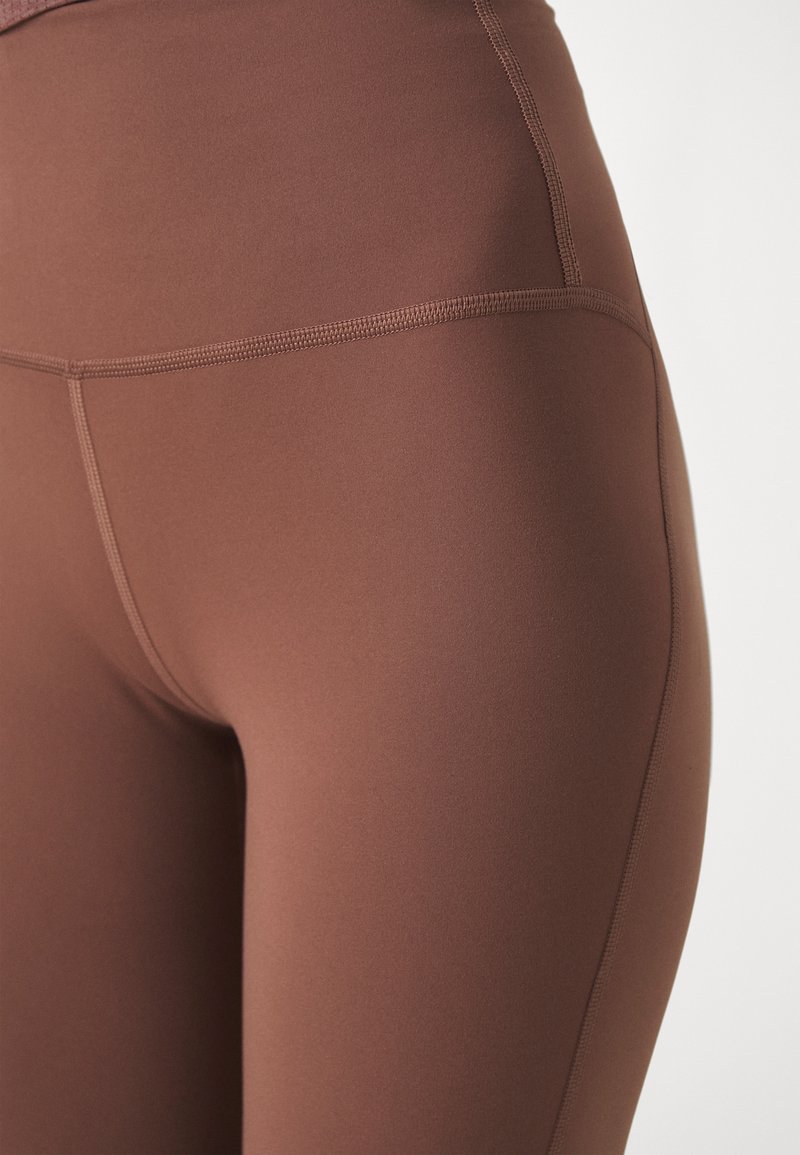Leggings de sport marron en tissu lisse et extensible, avec une taille haute et des coutures latérales sans couture pour un ajustement élégant.