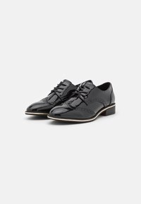Chaussures oxford en cuir verni noir avec détails en brogue, lacets plats et petit talon. Présentent une forme classique et une finition lisse et brillante.