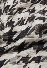 Strukturiertes Gewebe mit einem abstrakten Hahnentrittmuster in Schwarz, Grau und Creme, versehen mit verstreuten Strassakzenten.