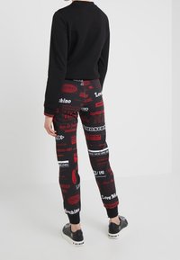 Czarny sweatshirt w połączeniu z wzorzystymi spodniami dresowymi z czerwonym i białym tekstem związanym z podróżami. Uzupełniony ściągaczami i butami z logo.