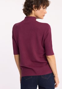 Sweter z krótkim rękawem i stójką z głębokiego fioletowego dzianiny. Rybakowe mankiety i detal w dolnej części, z luźnym krojem dla wygody.