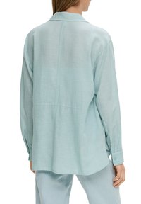 Camicia in lino azzurro chiaro con vestibilità rilassata, maniche lunghe e colletto a reverse. Presenta dettagli di cucitura e polsini abbottonati.