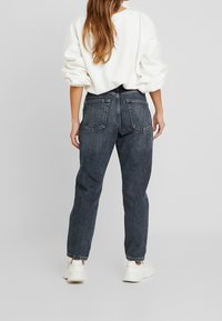 Tummanpesun farkut, joissa on korkea vyötärö, suorat lahkeet ja kaksi takataskua, yhdistettyinä rentoon valkoiseen huppariin ja valkoisiin lenkkareihin.