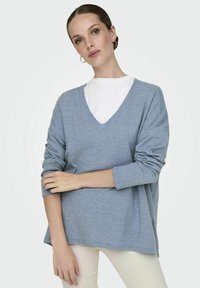 Maglione blu chiaro a V con maniche lunghe, vestibilità casual, tessuto morbido, sovrapposto a una camicia bianca. Dettaglio di cucitura discreto all'orlo.
