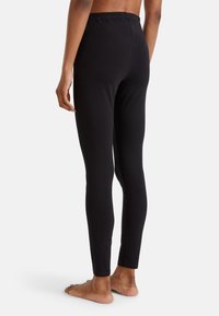 Leggings noirs avec un design ajusté et une taille élastique, vus de l'arrière. Le tissu semble lisse et extensible, avec un ourlet propre.