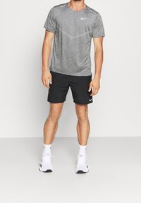 Grå Nike-t-shirt med korta ärmar och rund halsringning, i kombination med svarta shorts och vita sportskor, med subtila logotypdetaljer.