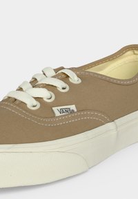 Μπεζ πάνινο παπούτσι Vans με λευκά κορδόνια, λευκή λαστιχένια σόλα και ορατά ράμματα στο πάνω μέρος.