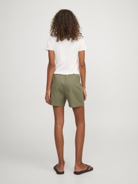 Bílý top s krátkým rukávem a vroubkovaným lemem, doplněný olivovými šortkami. Modelka ukazuje zadní pohled. Černé žabky dokončují outfit.