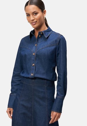 Camicia in denim scuro con colletto a punta, chiusura a bottoni e dettagli a yoke in stile western. Dotata di maniche lunghe e cuciture a contrasto.