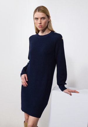 Knee-length temno-modra pletena obleka z dolgimi rokavi in okroglo izrezom. Ima zlate gumbe kot okras na rami. Gladka tekstura.