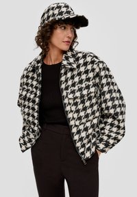 Czarnobiała kurtka w deseń houndstooth z zapięciem na zamek i kieszeniami z przodu, w zestawie z dopasowaną czapką. Teksturowany materiał i luźny krój.