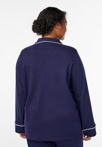 Maglietta da pigiama blu navy realizzata in materiale morbido, con maniche lunghe, colletto e bordo bianco lungo i polsini e il colletto.