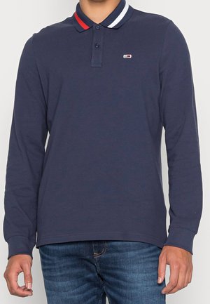 Navy pitkähihaine polo-paita, jossa on kaksinappinen kaulus, valko-punaisraitoiset kaulaklapit ja pieni emblem vasemmassa rinnassa. Puuvillakangasta.