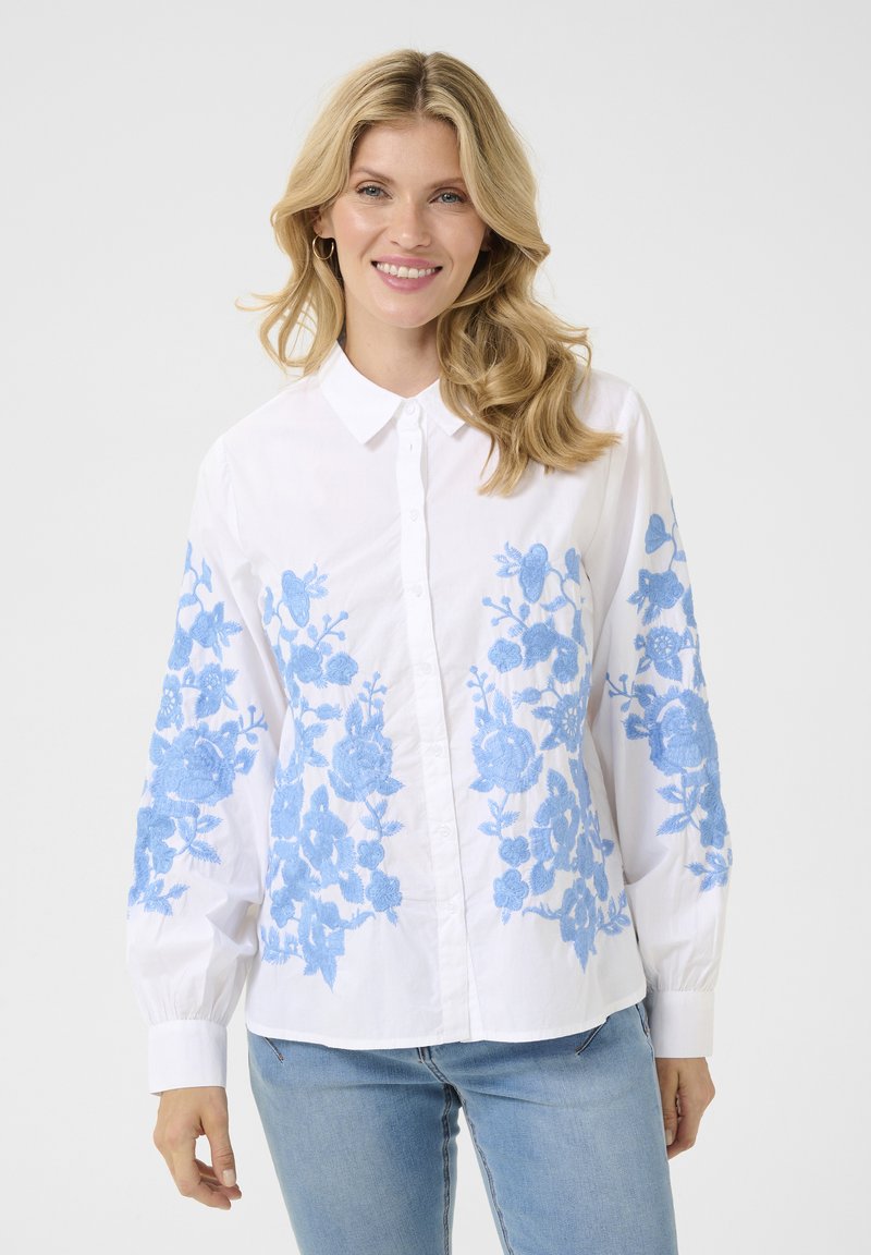 Camisa blanca de manga larga con bordado floral azul en las mangas, con un cuello clásico y mangas largas con fruncidos.