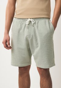 Pantalones cortos a rayas en verde y blanco, hechos de tela ligera. Presentan una cintura elástica con cordón y bolsillos laterales.