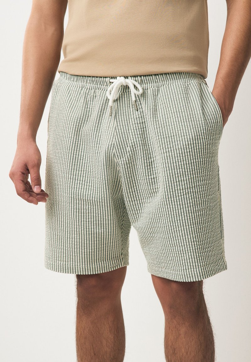 Pantalones cortos a rayas en verde y blanco, hechos de tela ligera. Presentan una cintura elástica con cordón y bolsillos laterales.