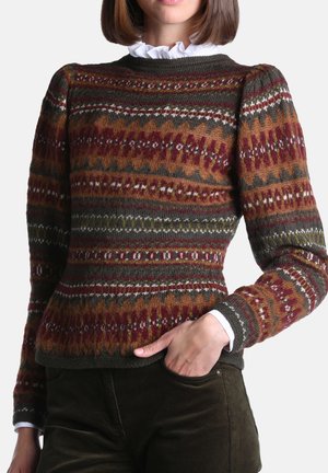 Femme portant un pull près du corps à motifs multicolores avec des épaules bouffantes et un chemisier blanc à col à volants en dessous.