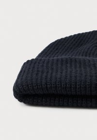 Pletená námořnická čepice s hřebíkovou texturou, s ohnutým lemem. Měkká tkanina, minimalistický design, žádné viditelné loga ani ozdoby.
