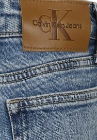 Pantalones vaqueros de mezclilla con un lavado azul claro y una textura sutil, etiqueta de cuero marrón cerca de la cintura grabada con "Calvin Klein Jeans".