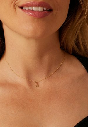 Collier pendentif en or avec une petite lettre « H », chaîne délicate, design ajusté et texture lisse au contact de la peau.
