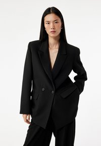 Sort dobbeltradet blazer med spidse slag, to forlommer og en afslappet pasform, med en glat tekstur og ingen synlige mønstre.