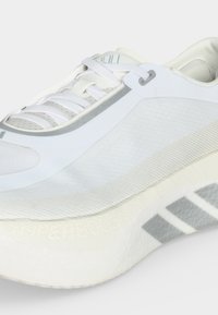 Λευκό και ανοιχτό γκρι αθλητικό παπούτσι με επάνω μέρος από δίχτυ, αφρώδη σόλα και κλείσιμο με κορδόνια, εμφανιζόμενο από πλάγια και εμπρόσθια γωνία.