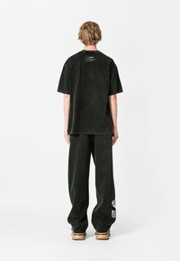 Camiseta negra de gran tamaño con una etiqueta rectangular en la parte posterior, combinada con pantalones anchos negros que presentan un diseño de calavera floral.