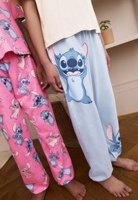 Kinder-Schlafanzughose aus Baumwolle in Rosa und Hellblau mit Cartoon-Stitch-Motiven. Die rosa Hose hat ein Muster, während die blaue Hose einen großen Aufdruck besitzt.
