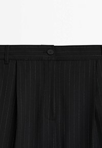 Pantalon noir à fines rayures, coupe ajustée, avec fermeture par bouton et passants de ceinture, montré de la taille vers le haut, vue de face.