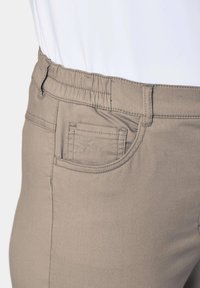 Beige katoenmix broek met een elastische taille, subtiele stikdetails en een klein zakje met een geborduurd ontwerp.