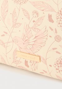 Kreemikas tekstuuriga kangas, millel on roosa kimalase ja lillemustriga ning kuldse ristkülikukujulise sildiga, millel on kiri "ANNA FIELD".