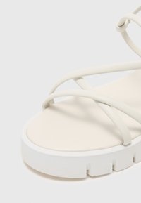 Sandale platform albă cu curele moi și ușoare. Talpa are un design masiv, cu caneluri pentru aderență. Textură netedă în ansamblu.