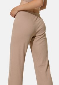 Pantalons larges côtelés beiges avec une texture douce et une taille élastique, présentant une silhouette épurée et un design minimaliste.