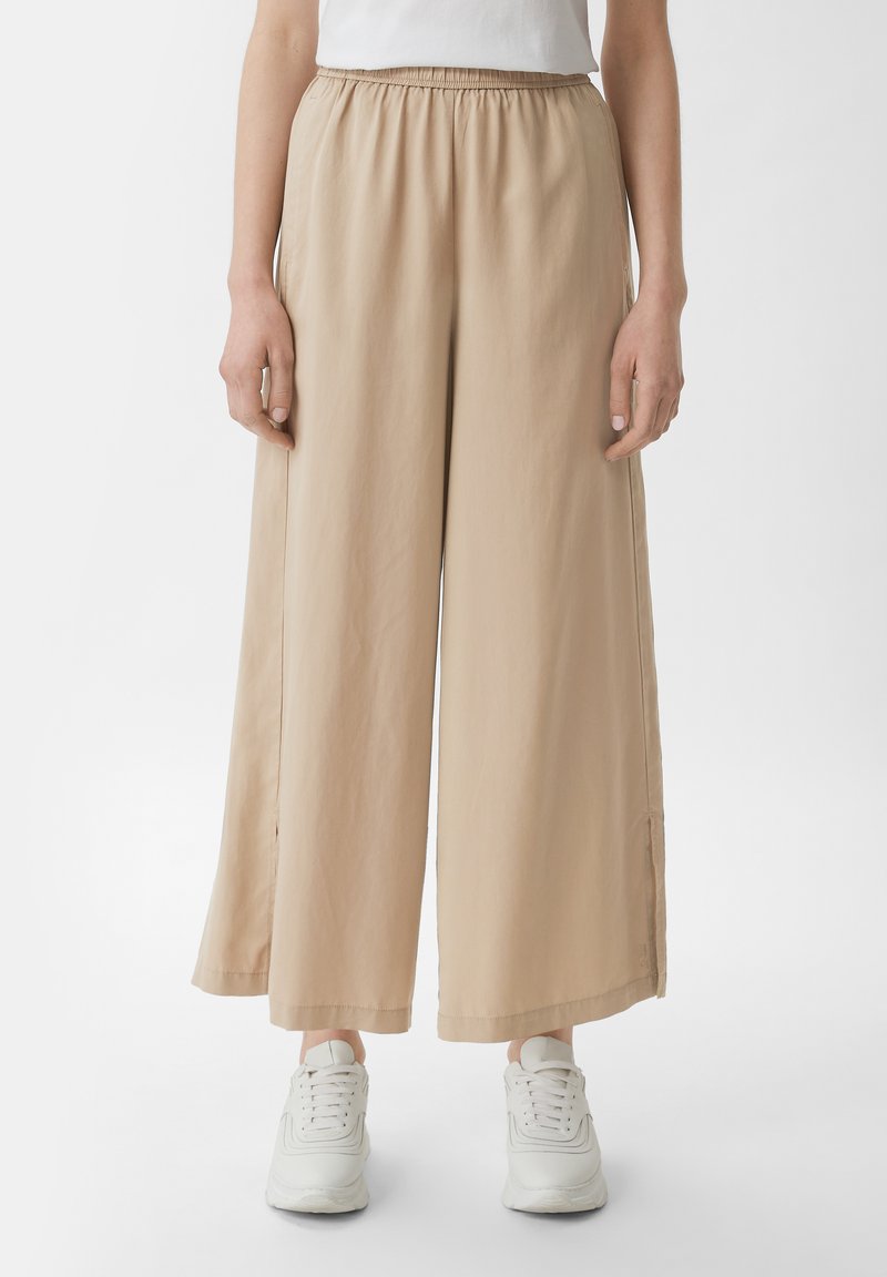 Beige weite Hose mit elastischem Bund, aus weichem Stoff und glatter Textur. Kombiniert mit weißen Sneakern.