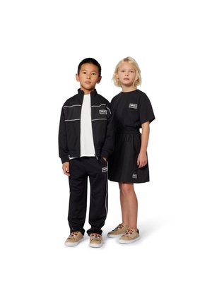 Survêtement noir avec des rayures blanches sur la veste et le pantalon; robe noire avec une taille élastique; chaussures beiges avec des motifs de tigre.