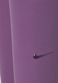 Fialové sportovní legíny s hladkým, pružným materiálem. Obsahují malé, lesklé logo Nike umístěné blízko dolní části.