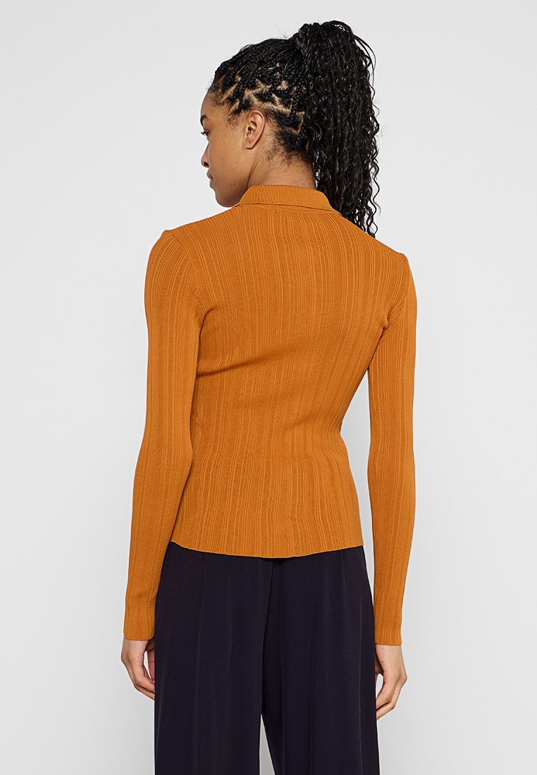 Langärmliges, geripptes Strickoberteil in verbranntem Orange mit figurbetontem Schnitt und Kragen. Glatte Textur, minimale Details und maßgeschneiderte Gestaltung.
