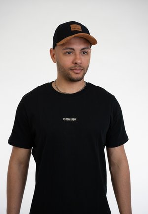 Black cotton t-shirt with small white "JOHNNY URBAN" text; paired with a black cap featuring a brown suede peak and a logo patch.