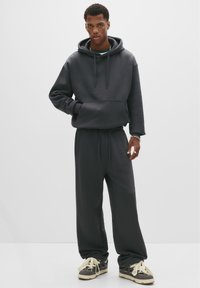 Dunkelgrauer Hoodie mit Kängurutasche, kombiniert mit passenden, locker sitzenden Sweatpants. Strukturiertes Material, Kordelzugbund und gedeckte Farben.
