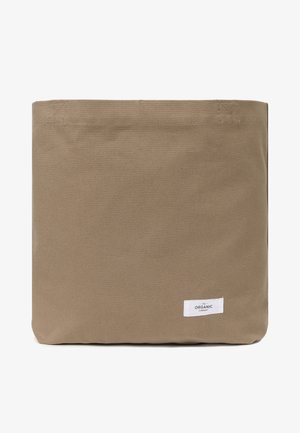Canvas-Tragetasche in erdigen Braun, rechteckige Form, mit strukturiertem Oberfläche. Kleines weißes Etikett mit der Aufschrift "The Organic Company" an der Seite.