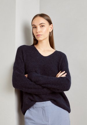 Mørk marineblå v-hals genser laget av et fluffy materiale, med lange ermer og løs passform, kombinert med lysegrå bukser.