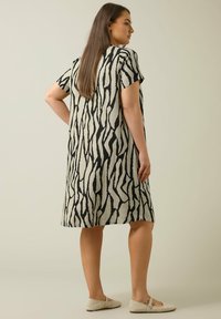 Kurzärmliges Kleid aus leichtem Stoff mit einem schwarzen abstrakten Muster auf beigem Hintergrund, lockere Passform, knielang und mit subtiler Textur.