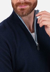 Pull en laine bleu marine avec un col demi-fermeture éclair, doté d'une doublure intérieure bleu clair et d'un tirette de fermeture éclair noire. Texture subtilement visible.