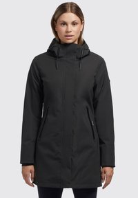 Veste noire imperméable avec capuche, zippers sur les poches latérales, design épuré et texture lisse. Mi-longue avec une coupe droite.