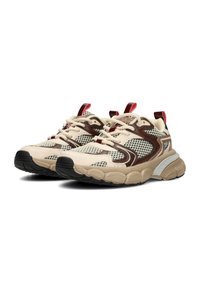 Sneaker in rete beige e marrone spessi, con lacci crema, suole spesse e texture, e linguette rosse su uno sfondo bianco.