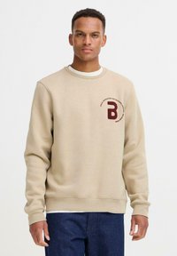 Felpa beige realizzata in tessuto morbido, con scollatura rotonda e polsini a coste. Un logo marrone scuro è ricamato sul petto.