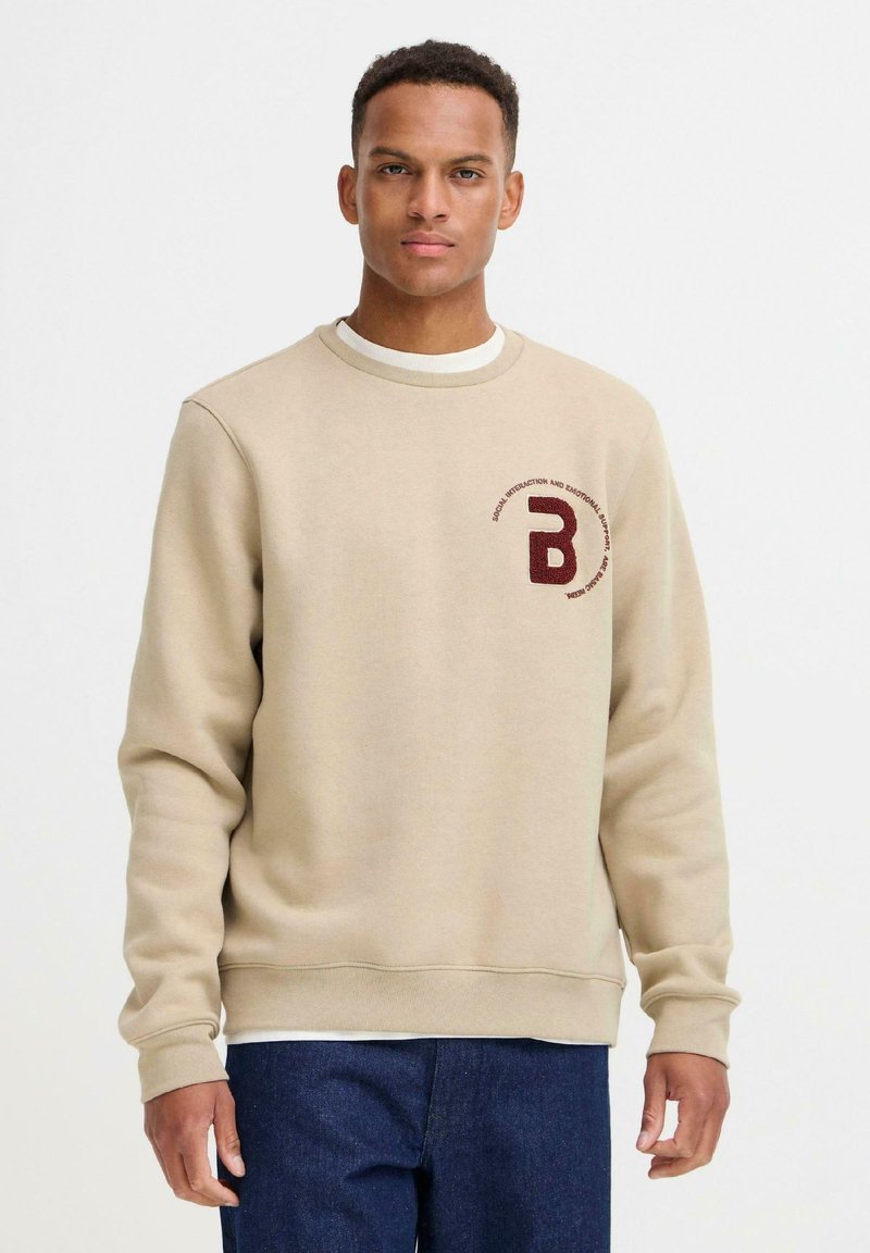 Felpa beige realizzata in tessuto morbido, con scollatura rotonda e polsini a coste. Un logo marrone scuro è ricamato sul petto.