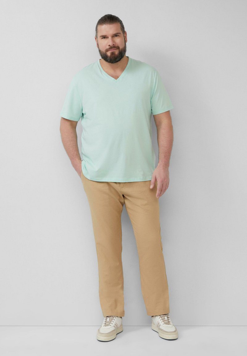 Mintgroene v-hals t-shirt, beige chino's en witte sneakers met lichtbeige accenten. Glad materiaal, relaxed fit, minimalistisch ontwerp.